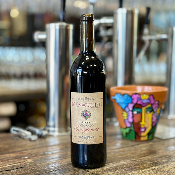 A bottle of Bonacquisti Wine Company 2023 Colorado Sangiovese sitting on the bar with a flower pot painted by Daniel Luna.