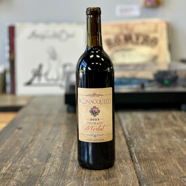 A bottle of 2023 Colorado Merlot from Bonacquisti Wine Company with a turntable and records in the background.