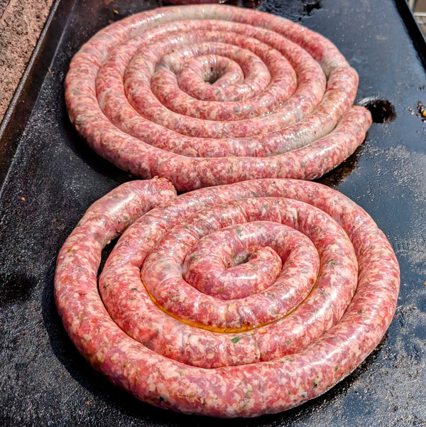 Two coiled raw sausages on a flat top grill surface