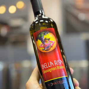 A hand holding a bottle of Bella Risa Sauvignon Blanc white wine, with a blurred kitchen background.