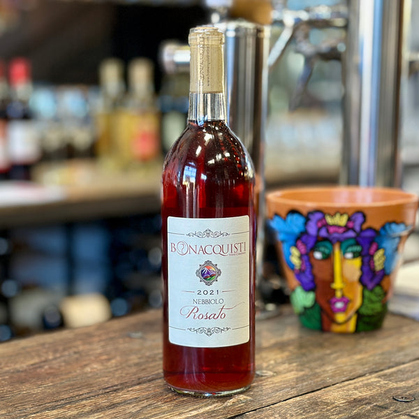 a bottle of Bonacquisti Wine Company 2021 Rosato Nebbiolo sitting on a bar with a Daniel Luna pot behind it.