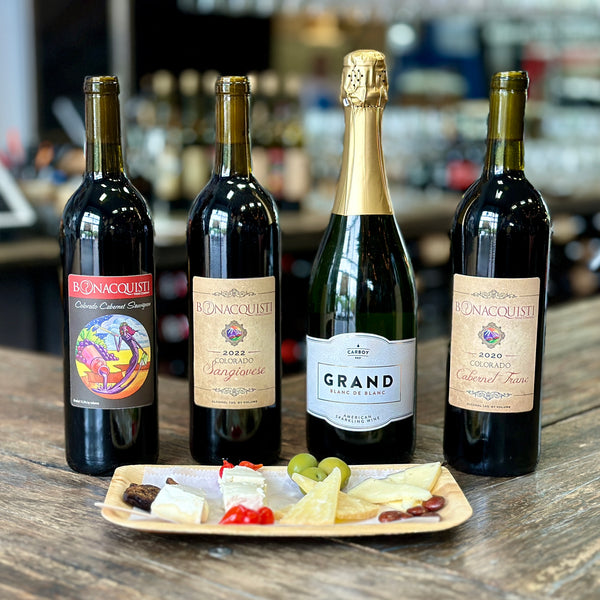four bottles of Bonacquisti Wine sit on the bar behind four cheeses.